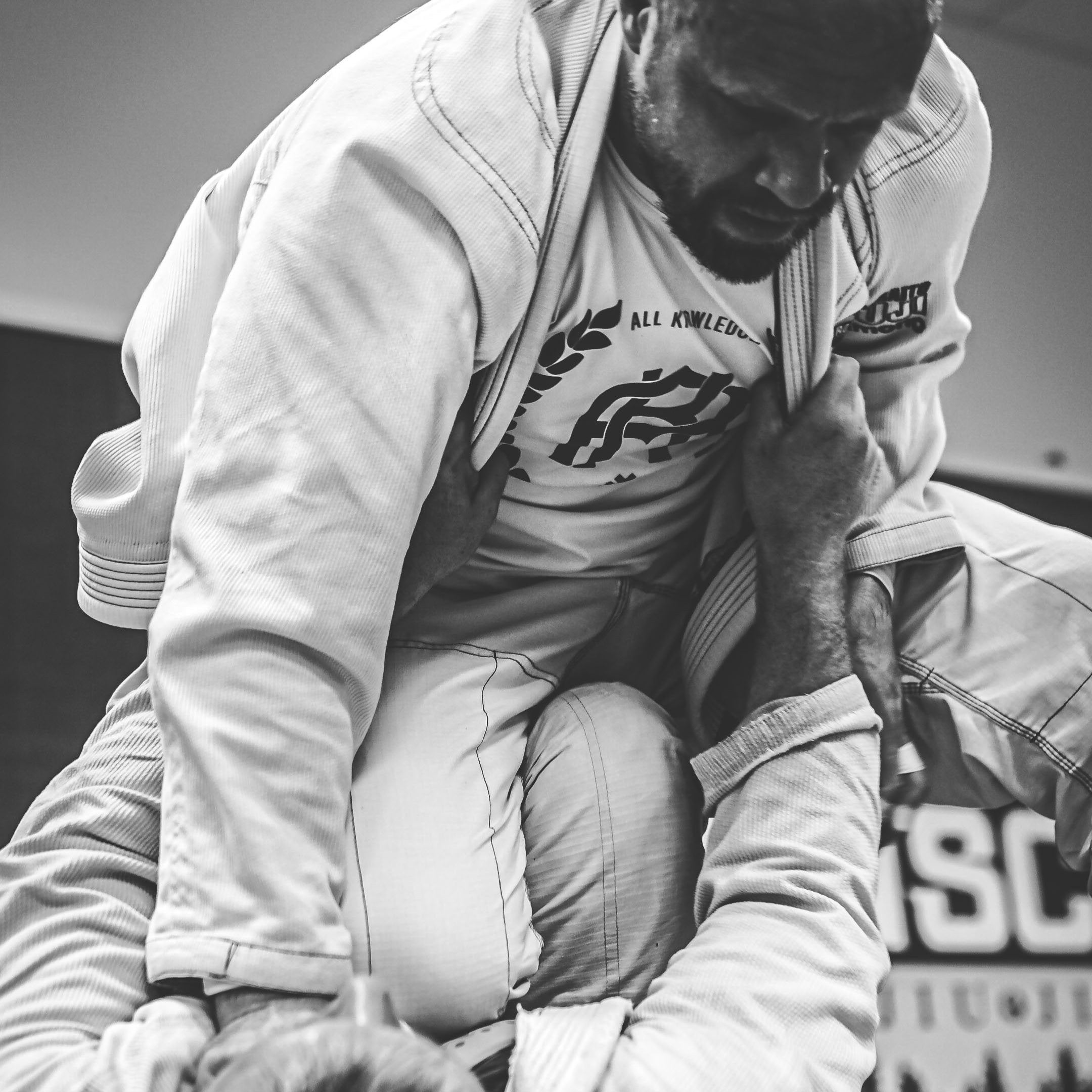 Two individuals wearing all knowledge in a martial arts or grappling position on a mat.