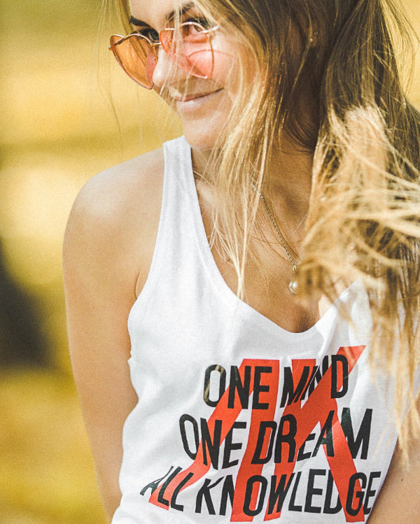 Woman wearing a white tank top with text, sunglasses, and blurred outdoor background